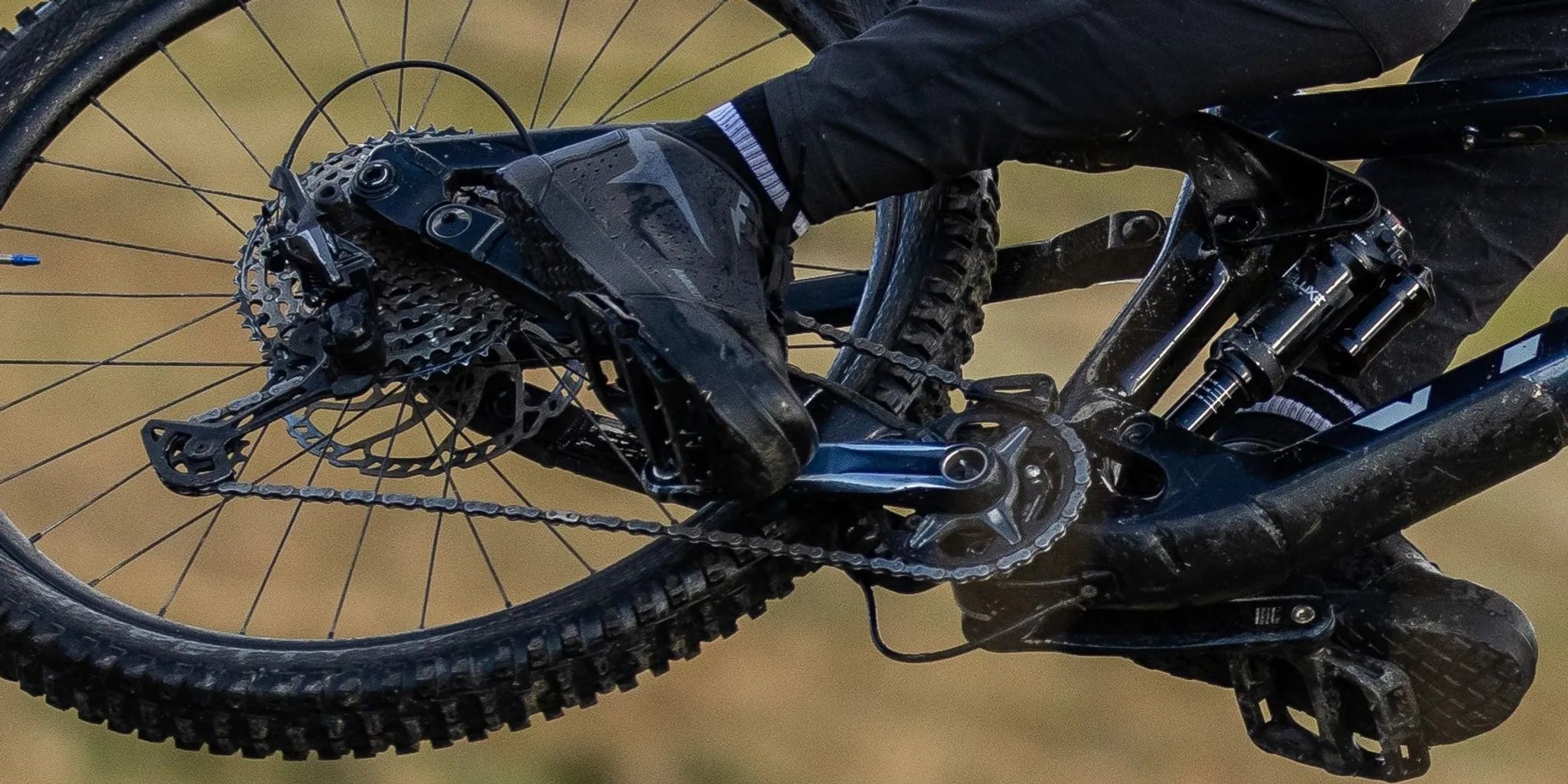 Close-up of a Pin-Lock 2.0 MTB shoe on a flat pedal showing the Hero Rubber™ outsole and wide toe box on a rocky trail