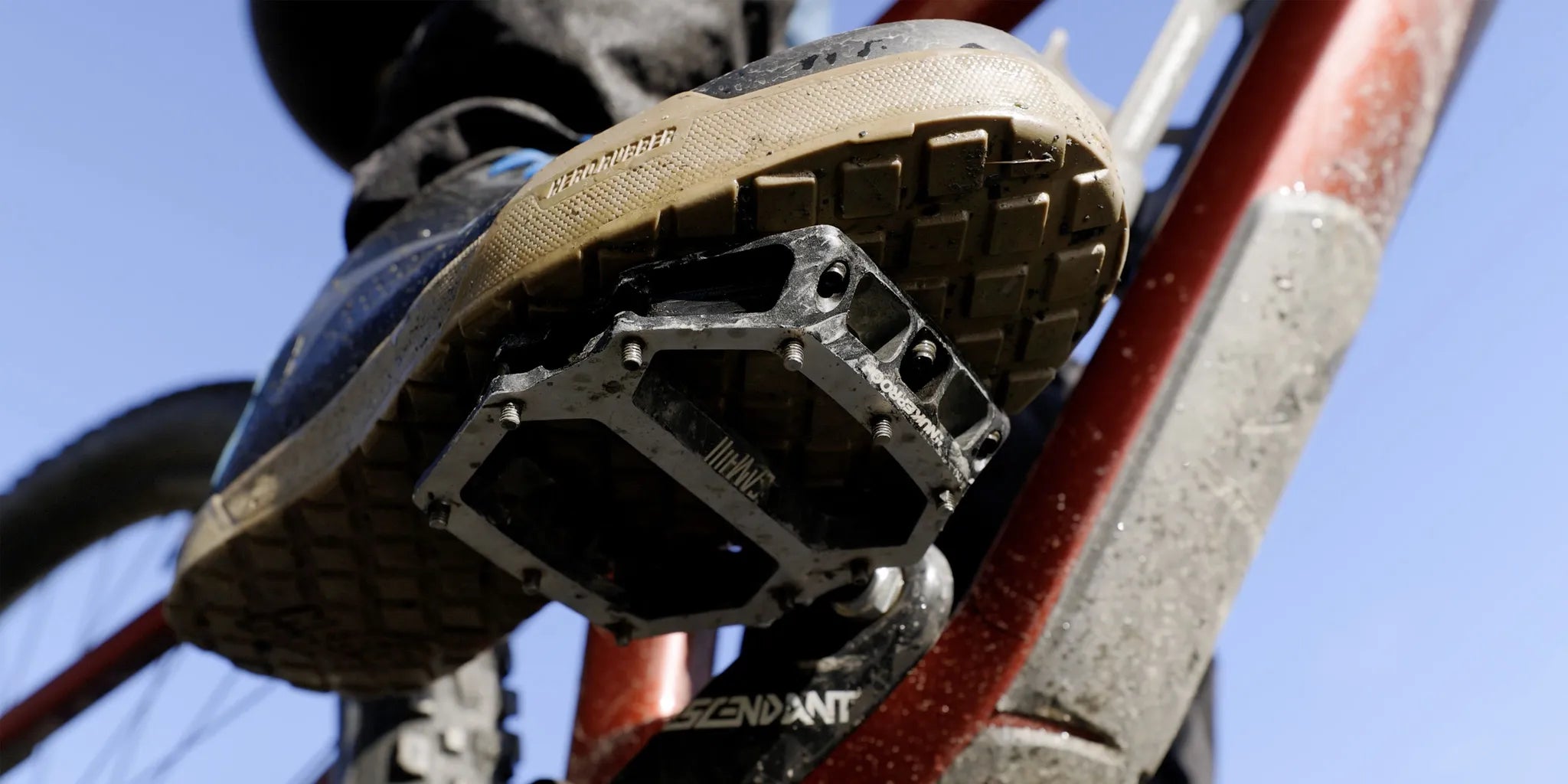 Wide fit flat pedal mountain bike shoe on a rocky trail beside a flat pedal