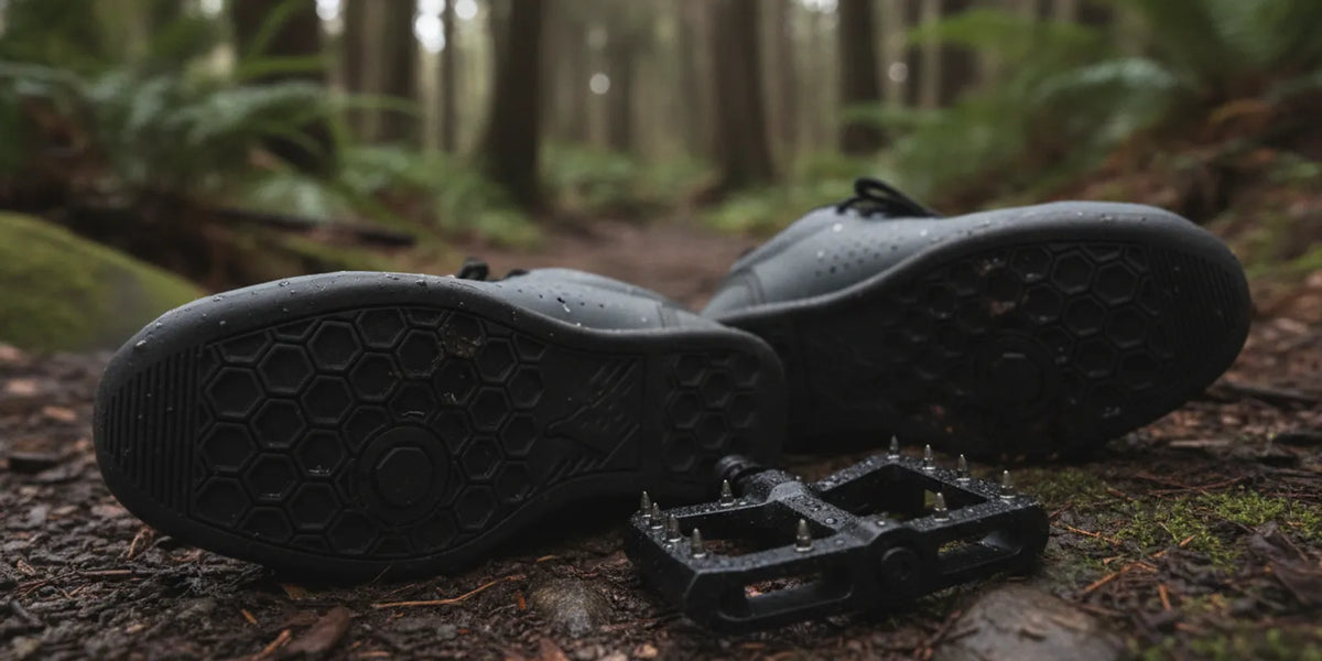 Flat-pedal mountain bike shoes resting on a rocky trail beside a bike pedal