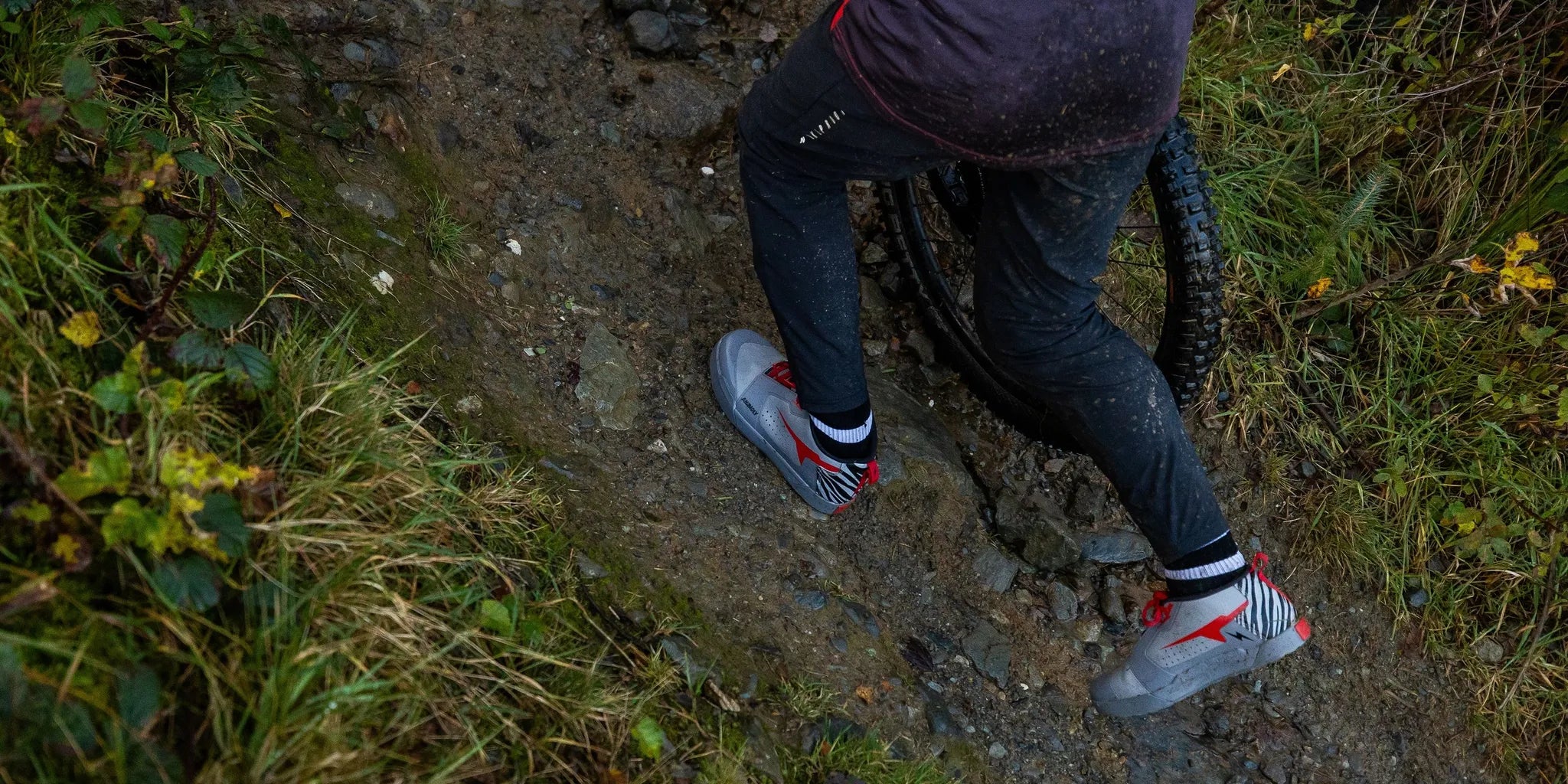 Mountain biker pushing a bike up a steep rocky trail in wide-fit MTB shoes with aggressive tread