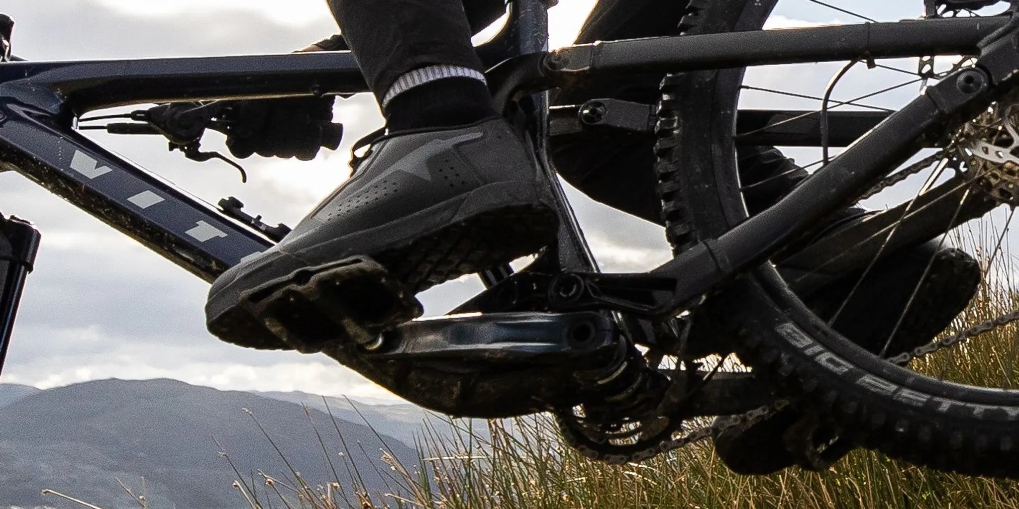 Premium technical flat-pedal mountain bike shoe resting on a damp granite slab along a trail